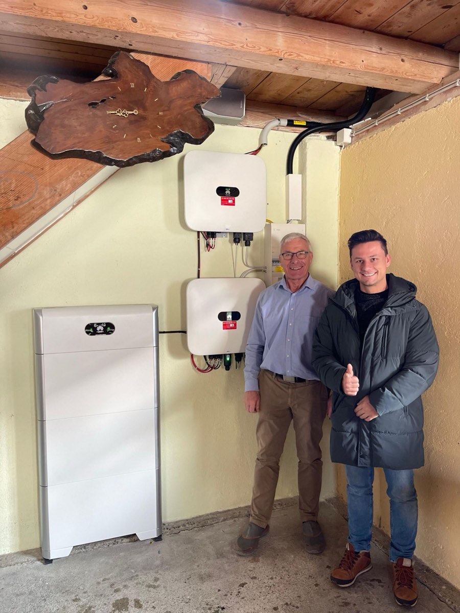 Hans Grossenbacher aus Dürrenäsch AG mit Daumen hoch neben seinem Runer-Berater vor dem frisch installierten Batteriespeicher mit zwei Wechselrichtern
